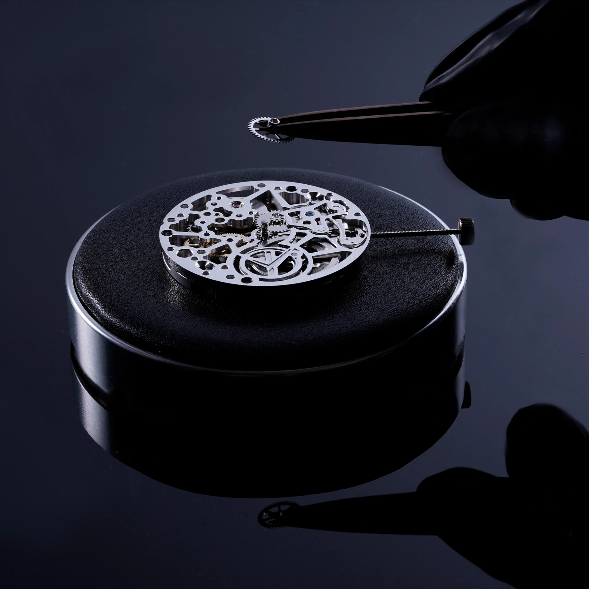 Close-up of a gloved hand placing a small watch component onto a watch dial during Swiss watchmaking assembly
