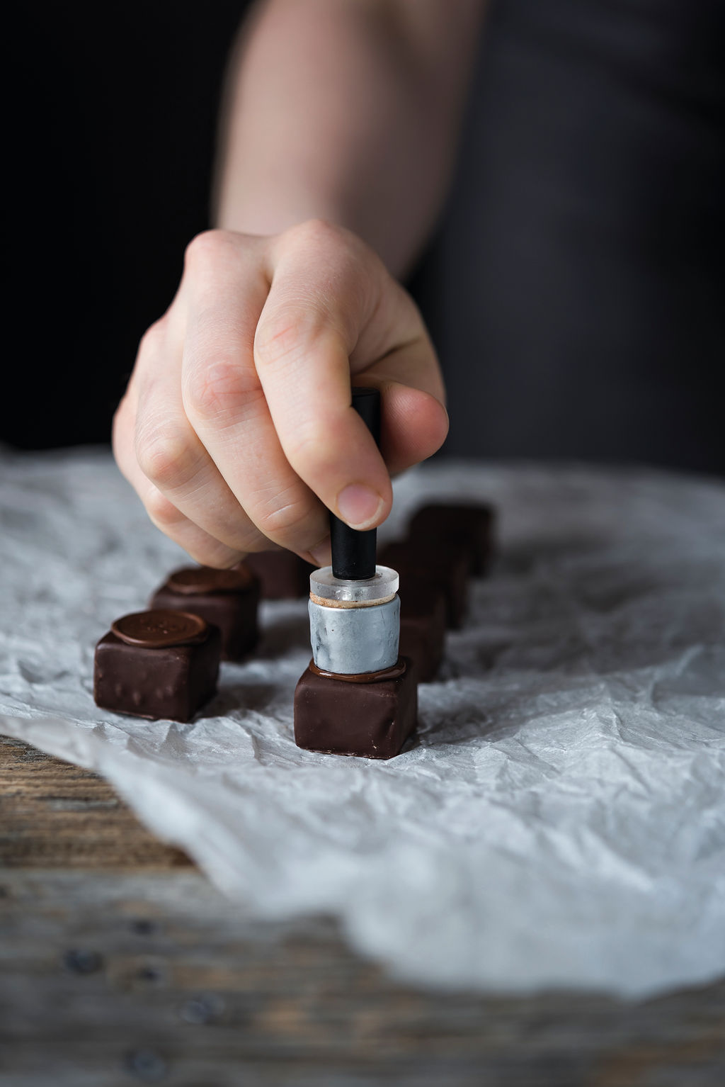 Hand using a professional stamp to mark a chocolate truffle alongside other freshly stamped truffles