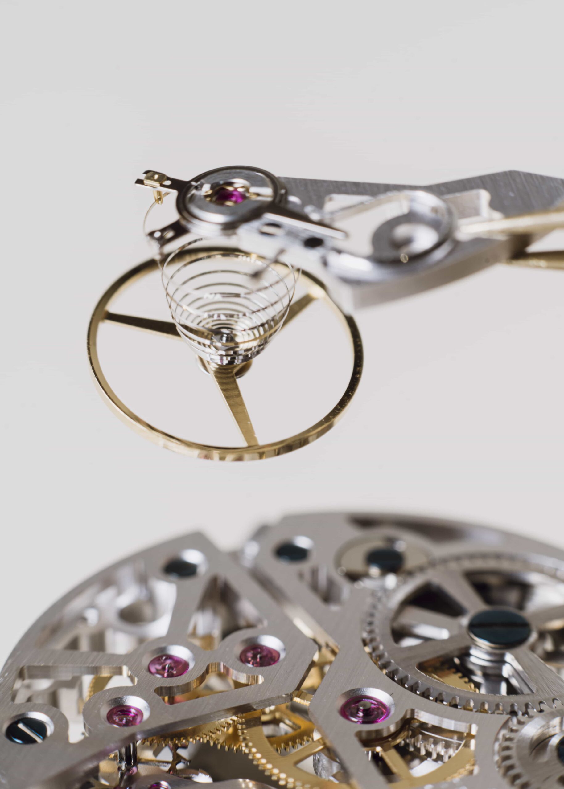Close-up view of a mechanical watch movement showing the balance wheel, hairspring, gears, and precision-engineered components during assembly.