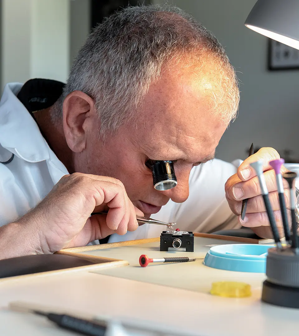 A skilled watchmaker wearing a magnifying loupe carefully assembles intricate watch components by hand at a traditional workbench.
