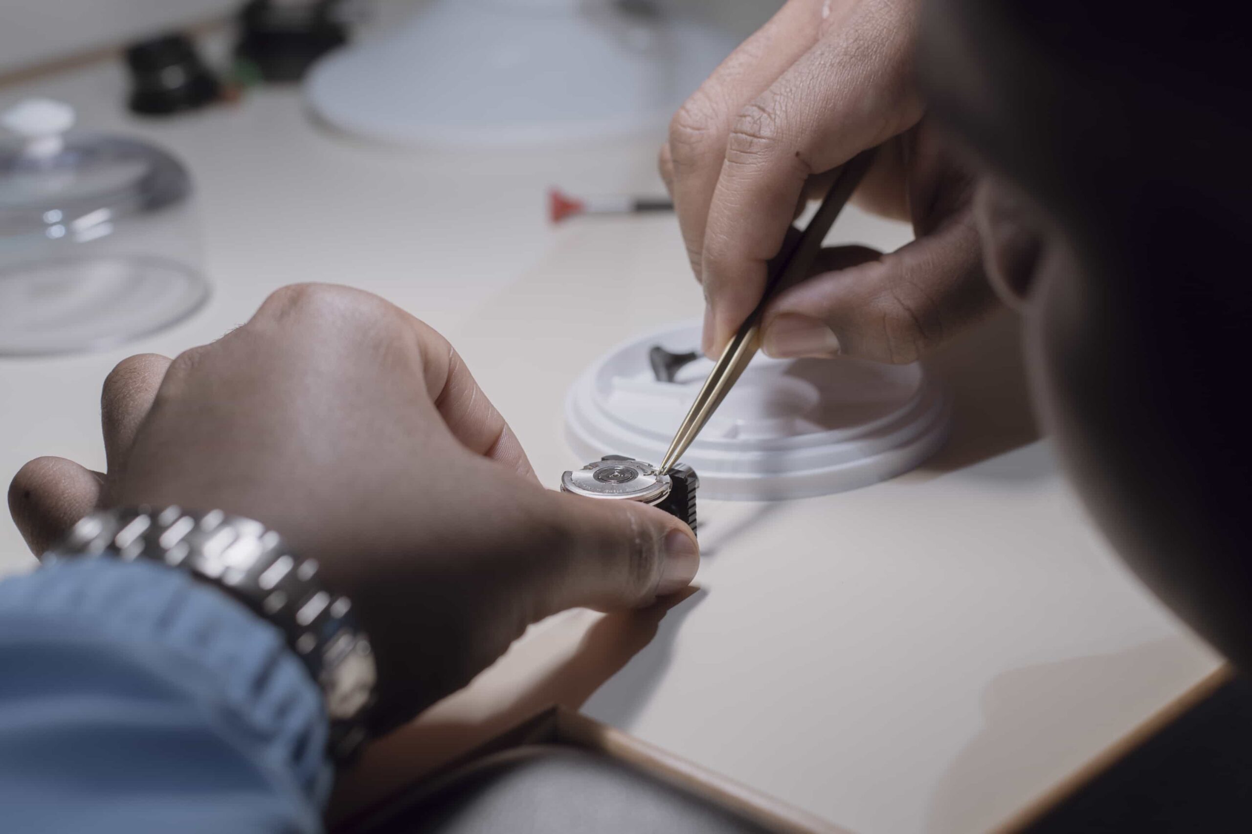 Watchmaker using precision tweezers to place a small mechanical part onto a watch dial in a Swiss workshop